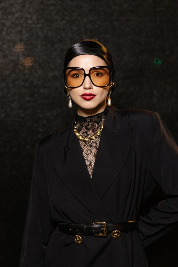 Street style at Paris Fashion Week: black double-breasted coat, gold logo lace top, orange sunglasses, Paris at night
