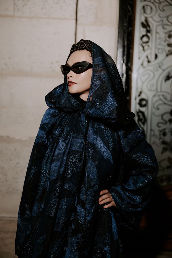Street style at Paris Fashion Week: navy hooded jacquard cloak, sunglasses, hotel interior, Paris
