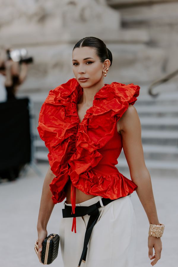 Portrait of a woman in red ruffled top, white trousers, black belt, show venue entrance, Paris