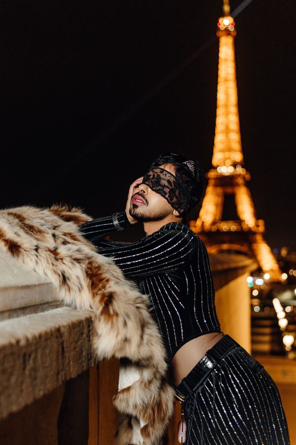 Portrait of a man in black pinstripe outfit, lace mask, cream fur coat, Eiffel Tower, Paris at night