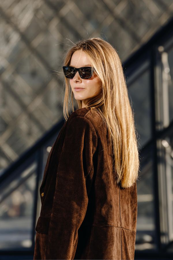 Portrait of a woman in brown suede jacket, black sunglasses, Louvre pyramid, Paris